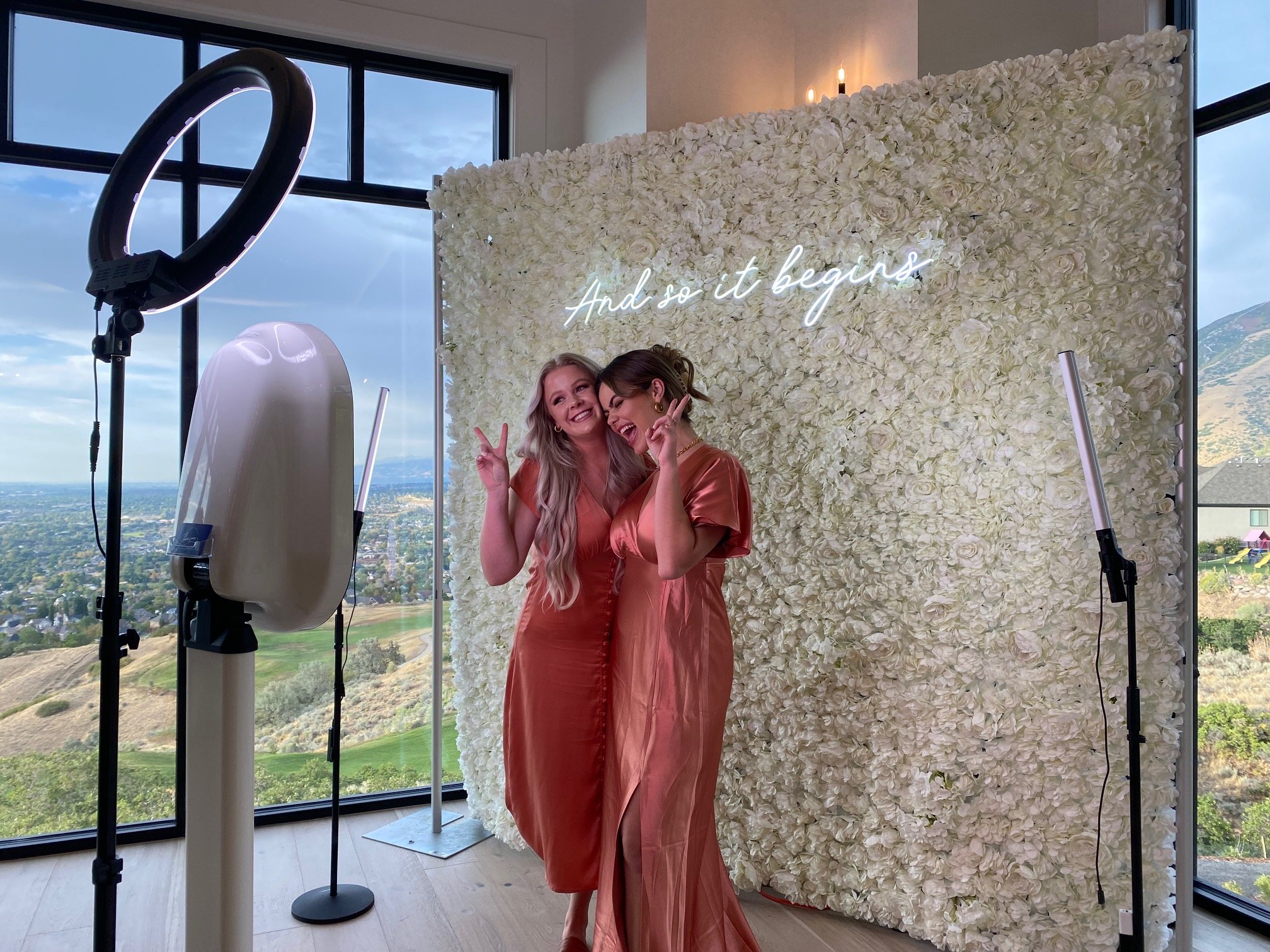 Two guests mid-session at the booth, in front of the white floral wall and neon sign