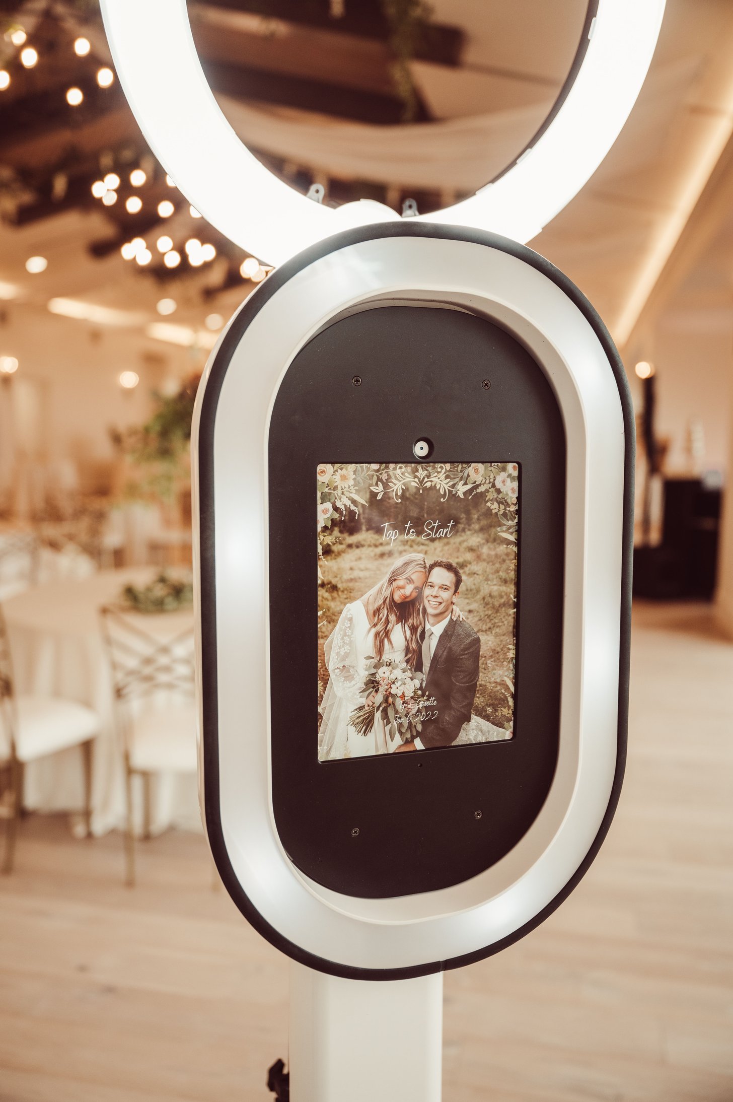 The photo booth standing in a reception hall with its ring light on and a portrait of a couple on the screen