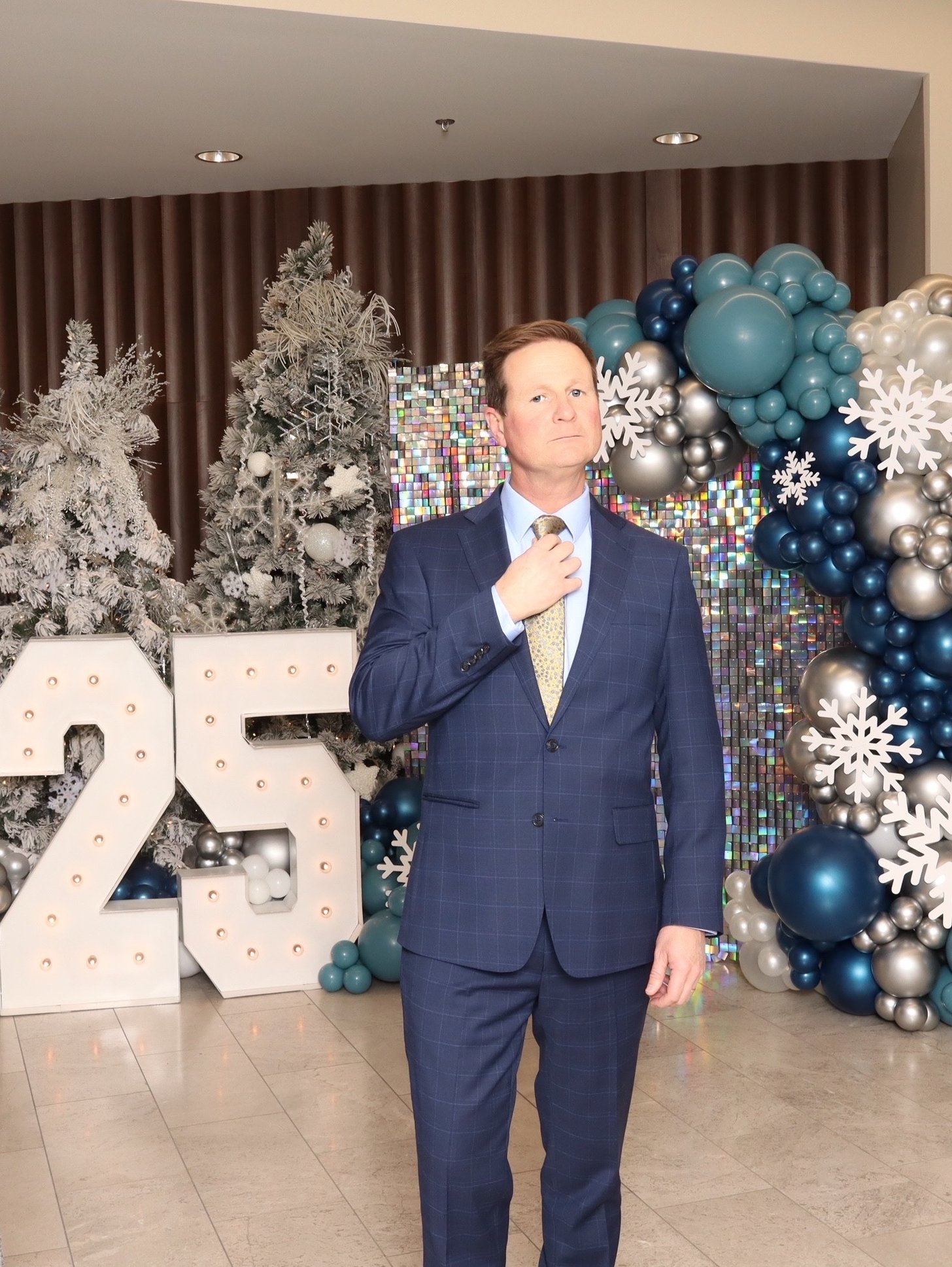 A guest beside a lit 25 marquee and balloon garland at a company party