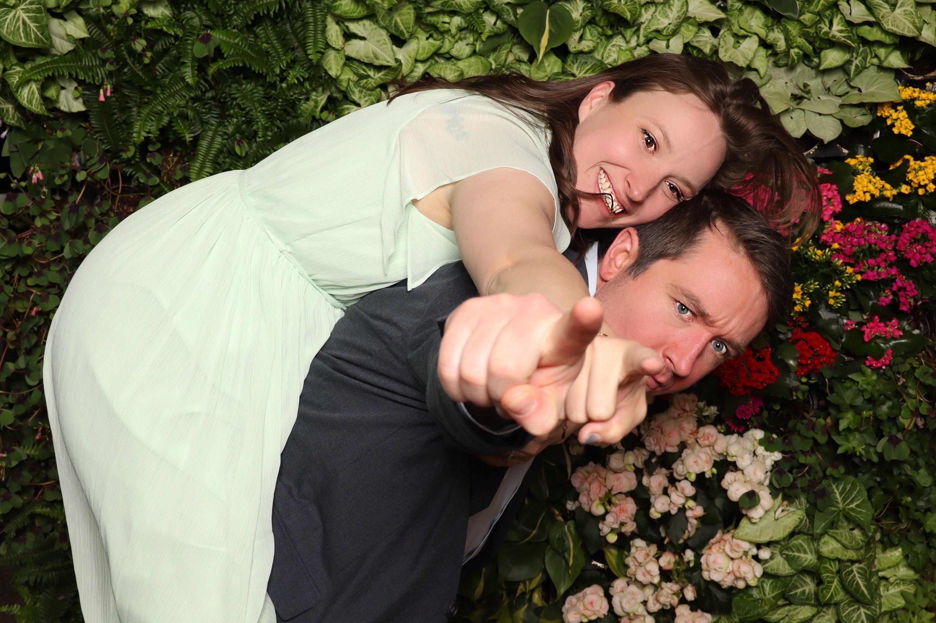 A couple laughing together in front of the greenery wall